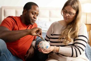 Man with woman putting money into piggy bank at home.