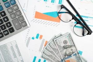 Financial documents, money, calculator, glasses and pencil on desktop.