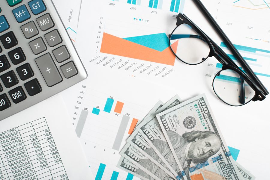 Financial documents, money, calculator, glasses and pencil on desktop.