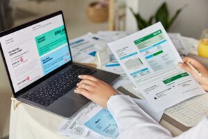 A person looking at a reports in a laptop and piece of paper.