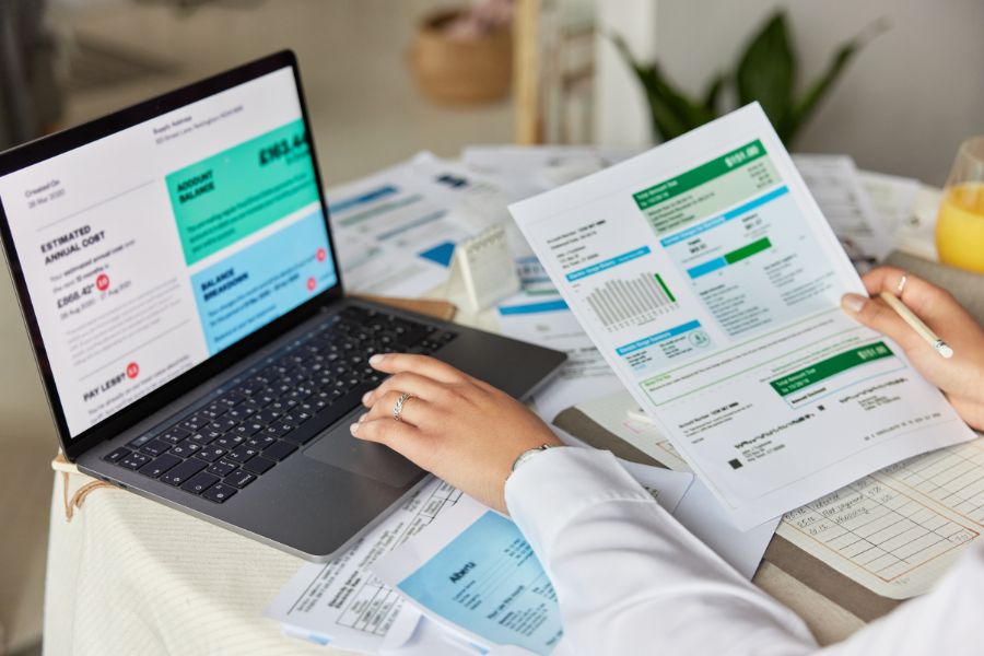 A person looking at a reports in a laptop and piece of paper.
