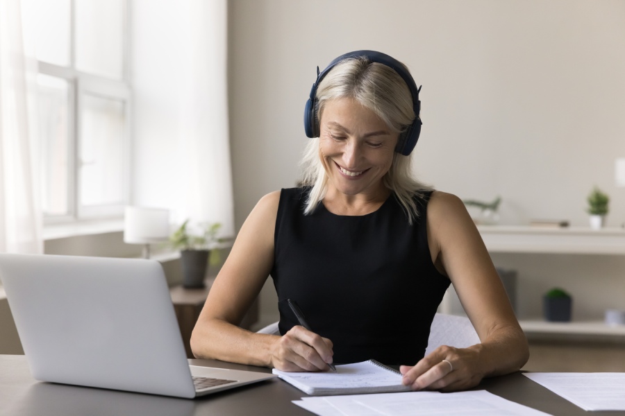 A woman working on table while listening to a call on her laptop.