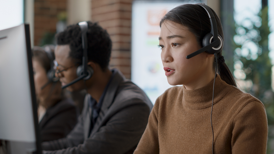 Telemarketing operator using headset to guide clients, helping with sales assistance and support at call center. Female employee talking to people on helpline, working at customer service.