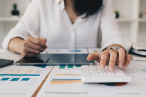 Business Woman or Accountant do math and analyze with calculator and paperwork on desk