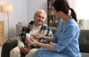 Female home care agency professional in blue scrubs assisting an elderly woman with medication management, illustrating the reliability and professional oversight of hiring a managed caregiver.