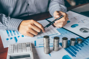 A business man analyzing financial reports with stack of coins and calculator.