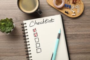 Checklist with marked checkboxes, coffee, plant and stationery on wooden table