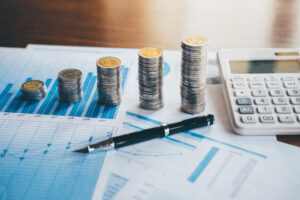 A stack if coins, calculator and a pen placed on top of accounting reports.