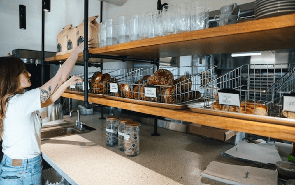 Small bakery staff arranging fresh bagels in an open retail layout that encourages interaction and experiential shopping.