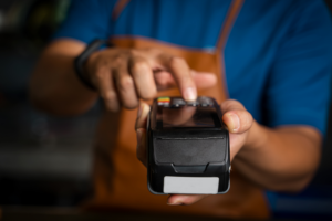 A person in an apron holding a credit card terminal and entering a transaction amount.